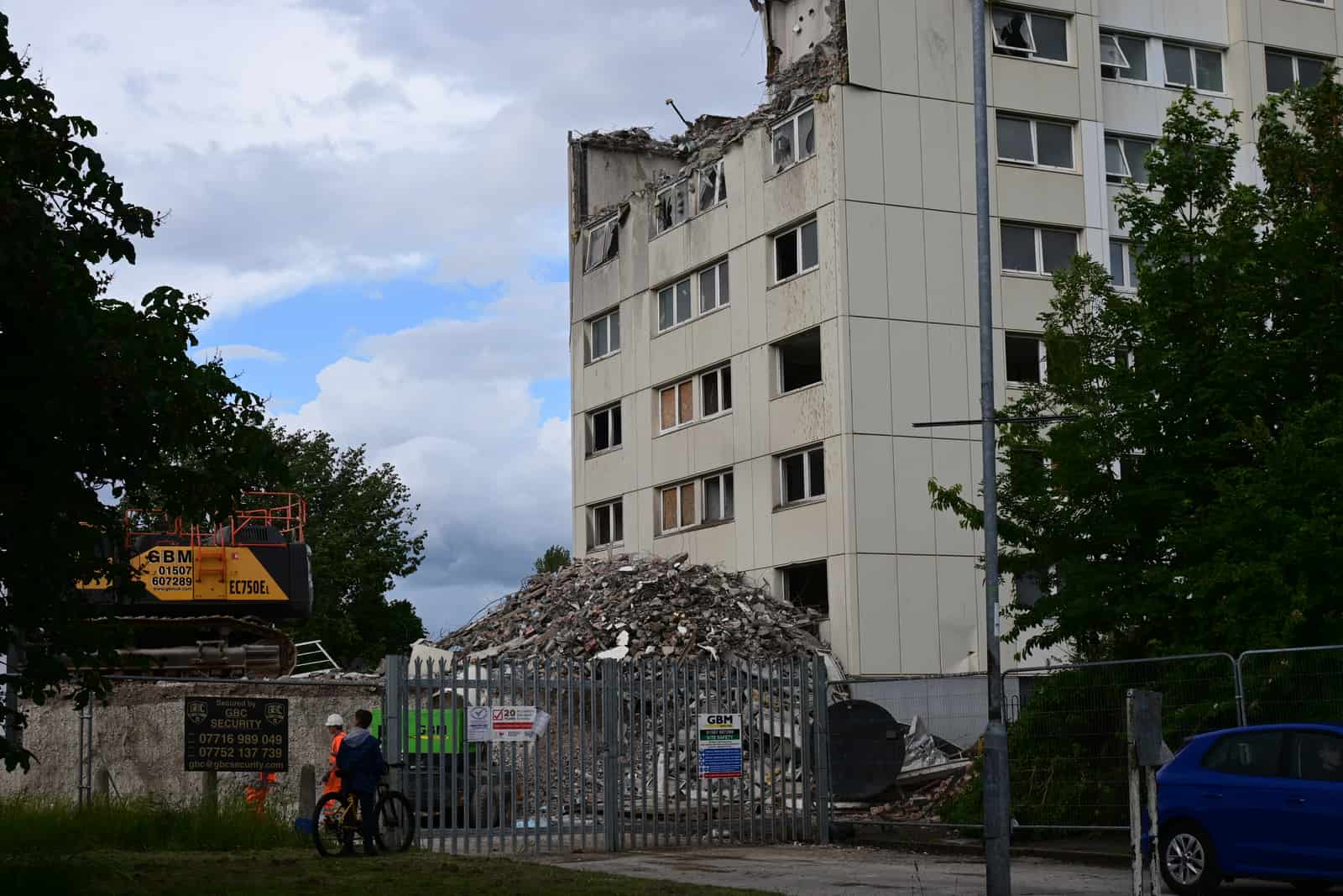 A large pile of demolition rubble beside a partially demolished building with plant working nearby, illustrative stock photograph