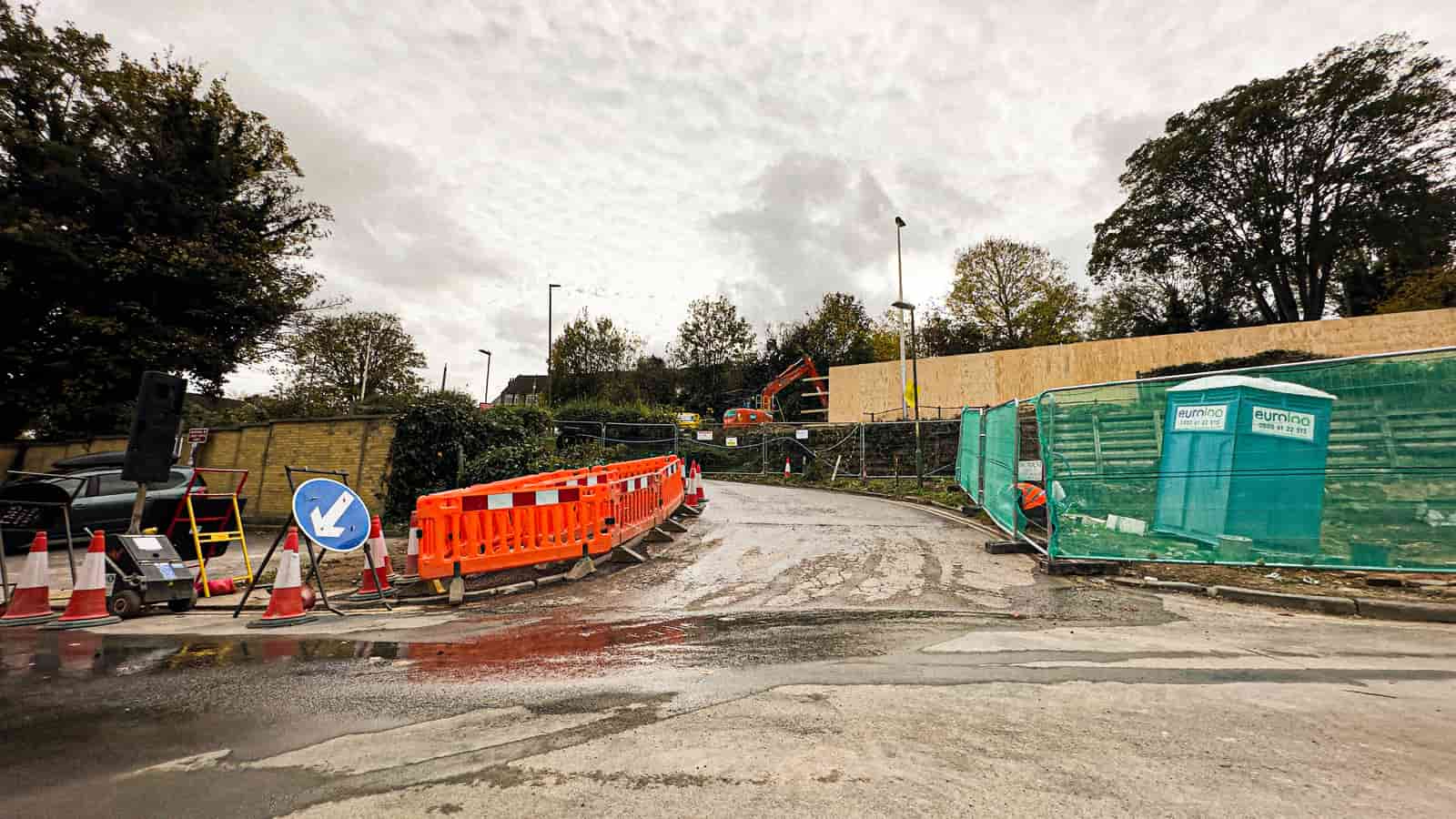 Groundwork under way on a fenced construction site with a portable restroom positioned beside the temporary barriers, illustrative stock photograph