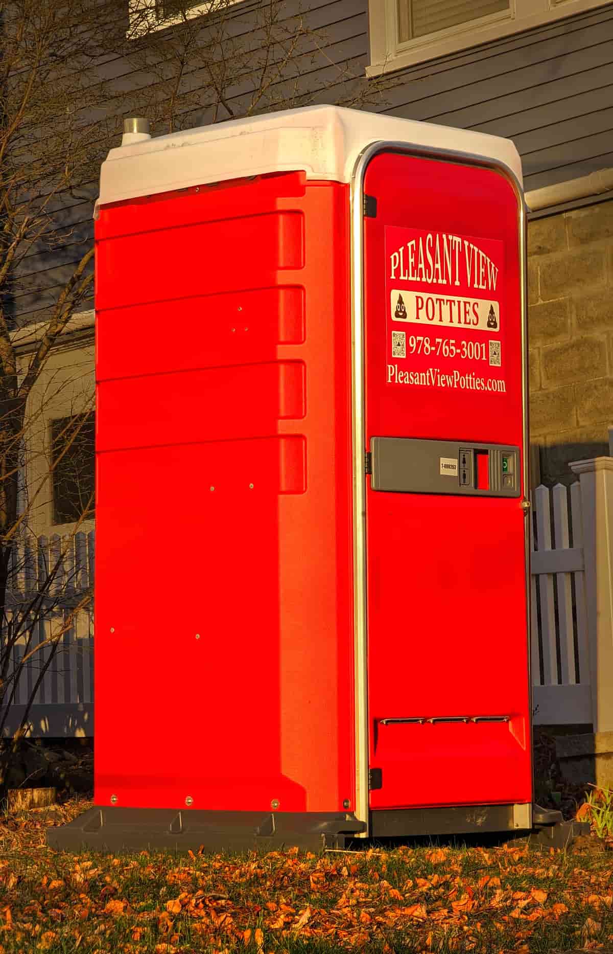 A single standard portable restroom unit standing on a paved surface beside a kerb, illustrative stock photograph